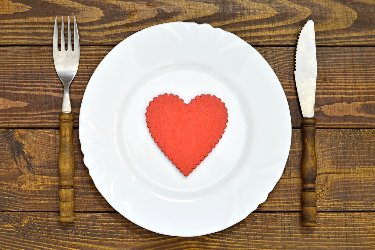 A dark wood table with a fork, knife, and white plate. A red heart is in the center of the plate
